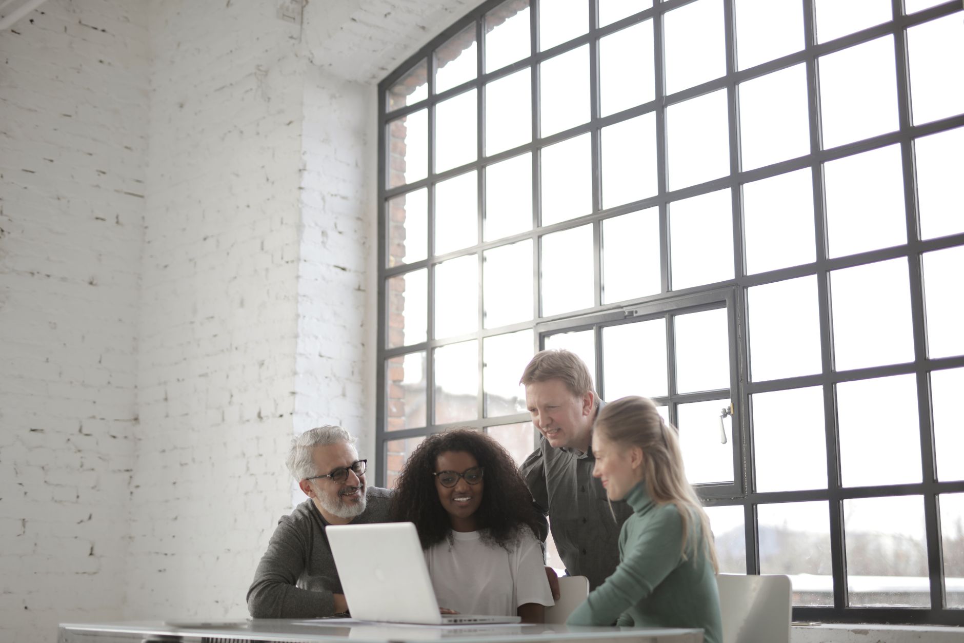 Focused coworkers gathering around a table with a laptop, reviewing marketing work